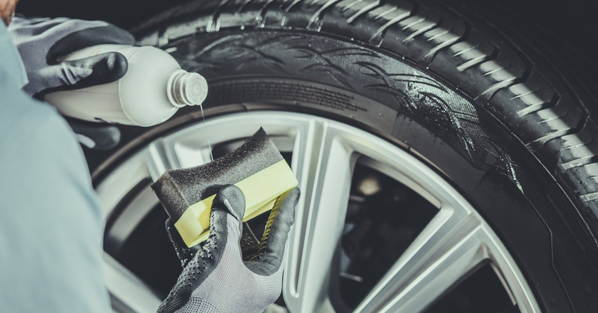 A person wearing gloves applies a liquid to a sponge to put on a tire. The tire already has some of the liquid on it.