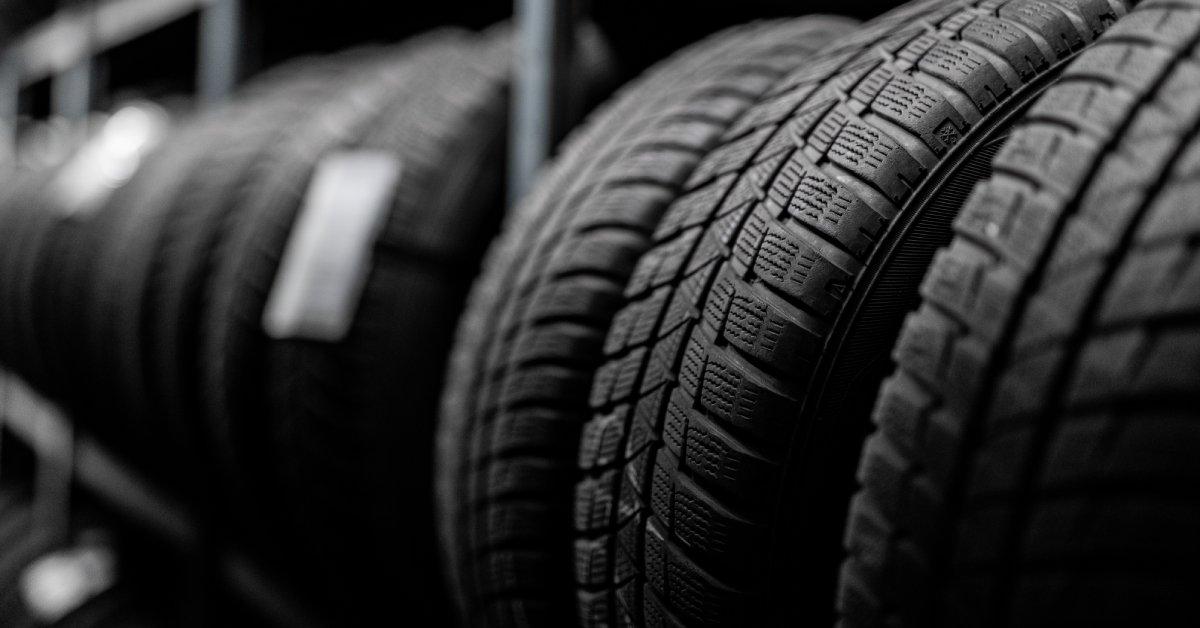 A group of brand-new, clean tires on a long shelf, with other tires behind them that are blurred out.