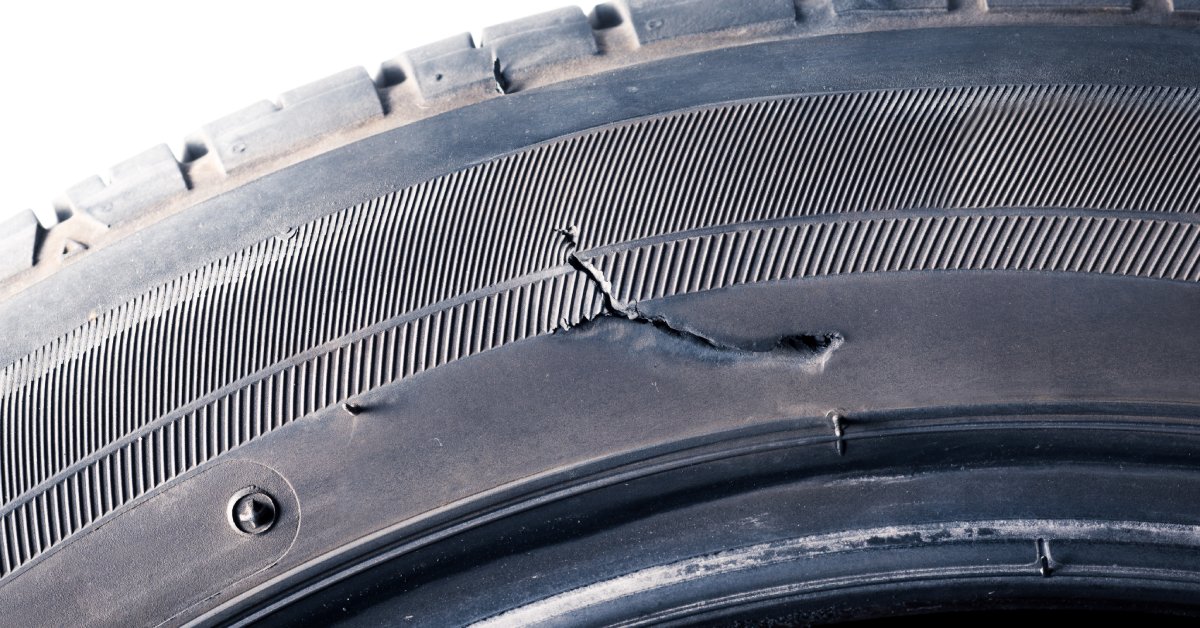 A detached tire that has a visible tear in the sidewall above the rim. It also has dirt on the tread.