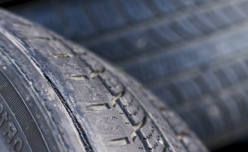 A car tire with small dirt markings on it. There are also signs of damage to the outer edge of the tire.