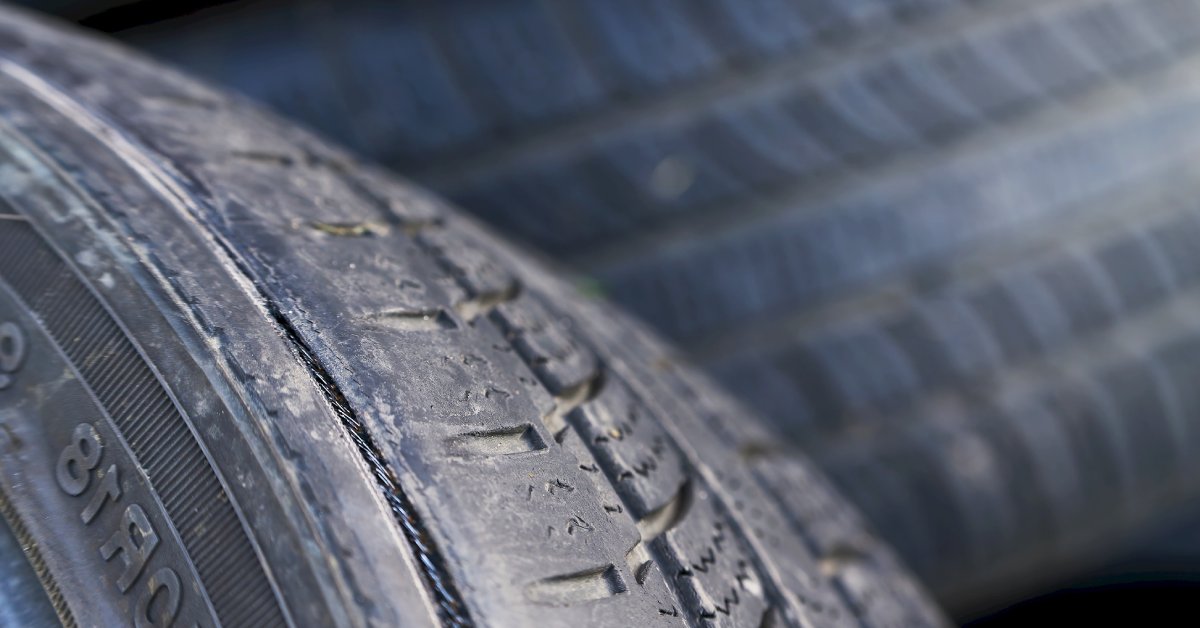 A car tire with small dirt markings on it. There are also signs of damage to the outer edge of the tire.