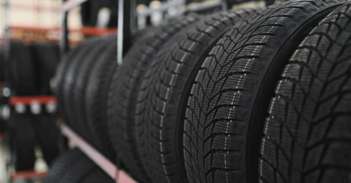 A tire shop with multiple tires stacked on a shelf close together. There are other shelves in the background.