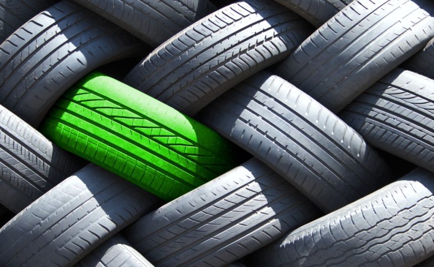 A stack of tires sitting on top of each other. One tire is green, while the others are their normal black color.