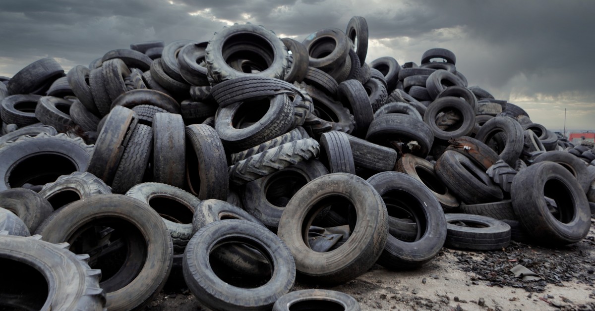 A tall pile of tires in an industrial landfill. There are a variety of tire sizes and types in the pile.