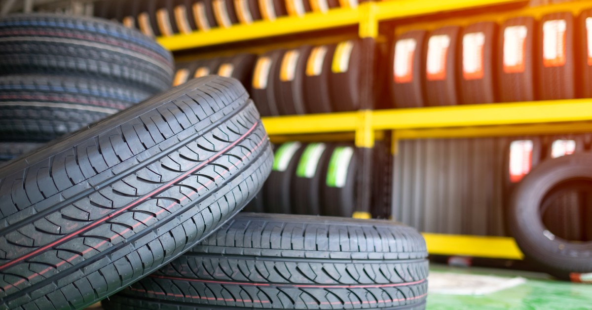 Two tires in a stack, with one on the floor and the other tilted above it. A shelf of tires is in the background.