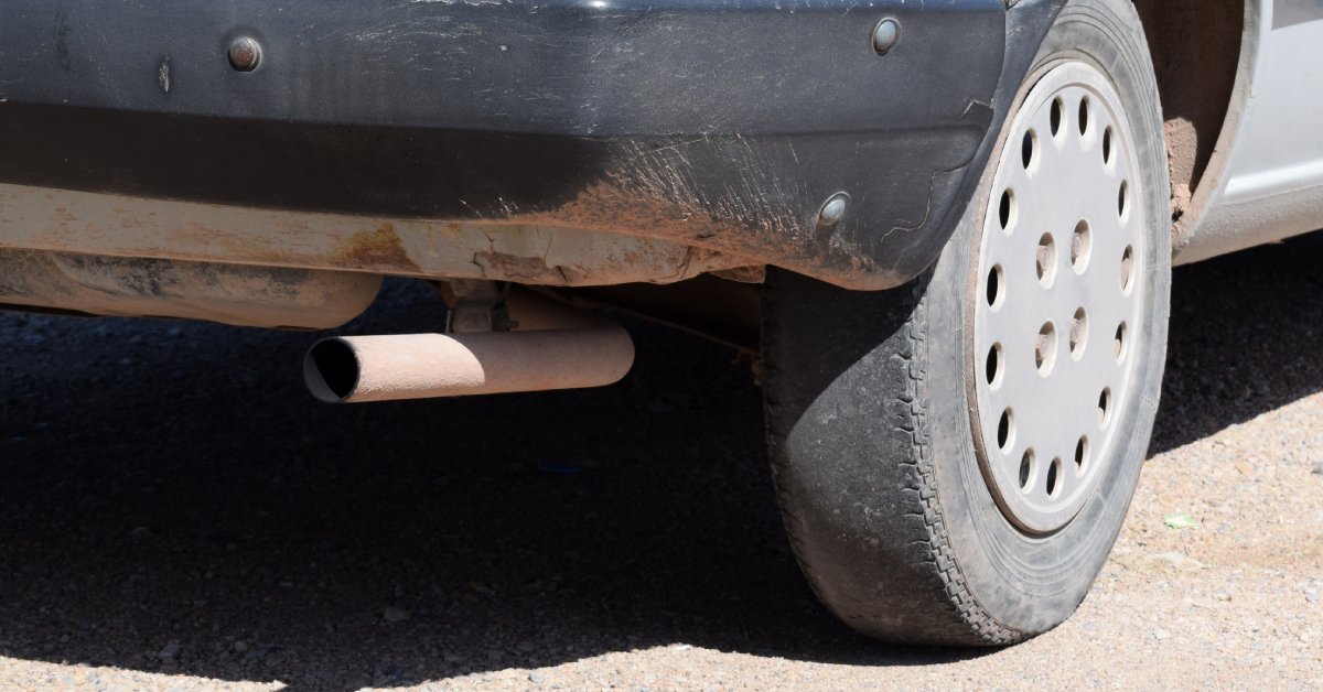The rear of an older vehicle with a tire that has dangerously worn-out tread that can lead to an accident.