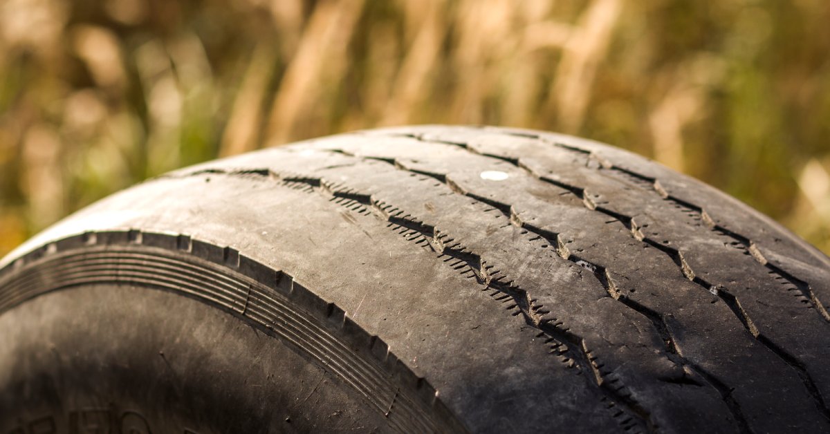 A car tire in warm light with worn-out tread that only has a few visible grooves on the top of the tire.