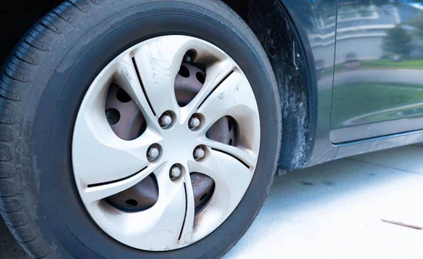 The tire of a car with clear lug nuts along the metal component of the wheel. The tire is slightly worn out.