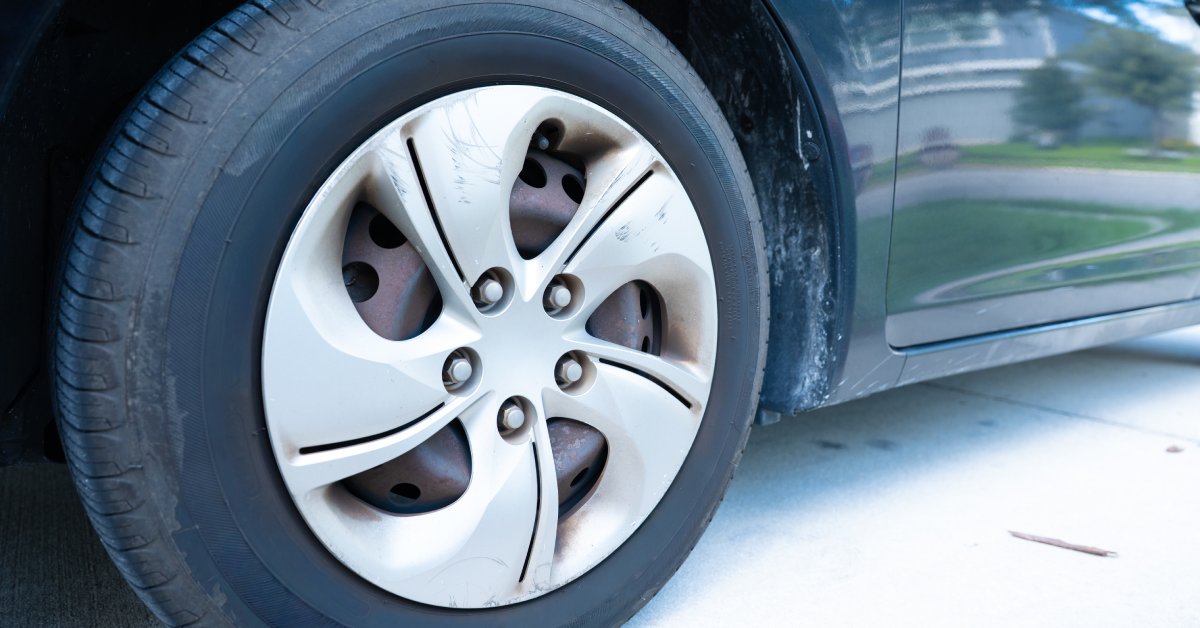 The tire of a car with clear lug nuts along the metal component of the wheel. The tire is slightly worn out.