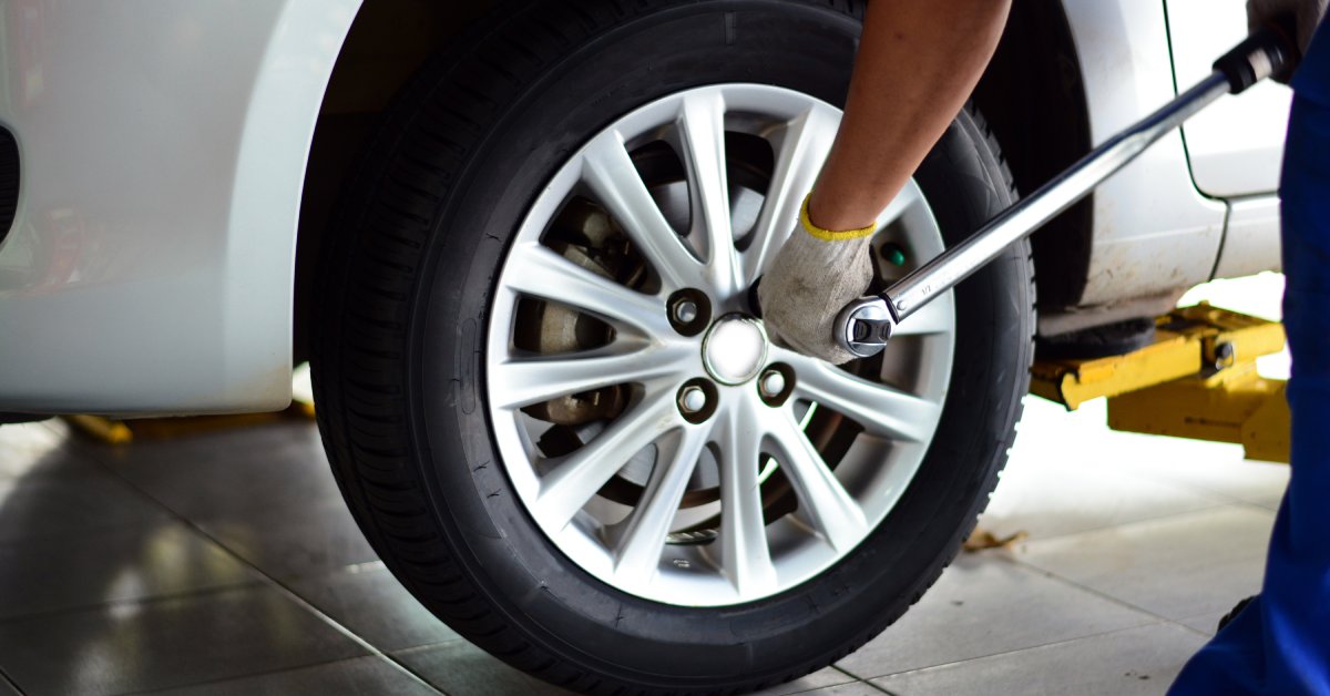 A person wearing white gloves is tightening the lug nuts on a tire. The tire is attached to a white vehicle.