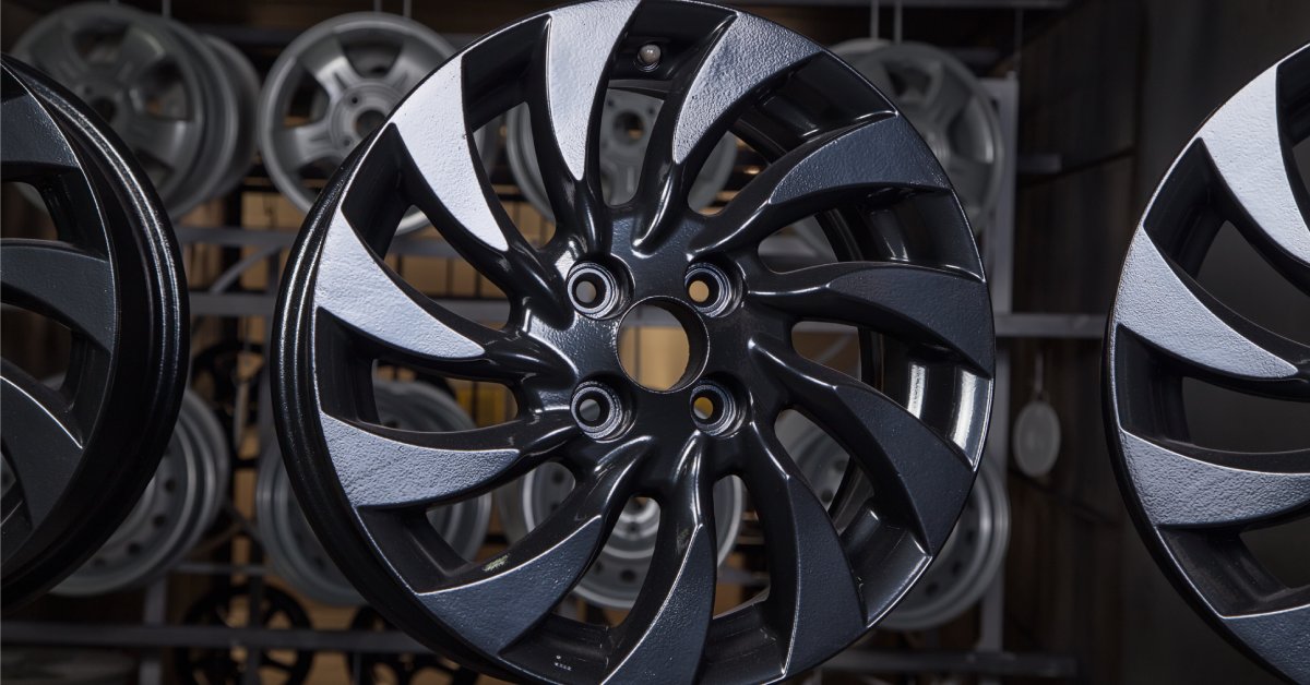 A black disk of a wheel hanging to dry after being powder-coated. Other disks are hanging behind the main one.
