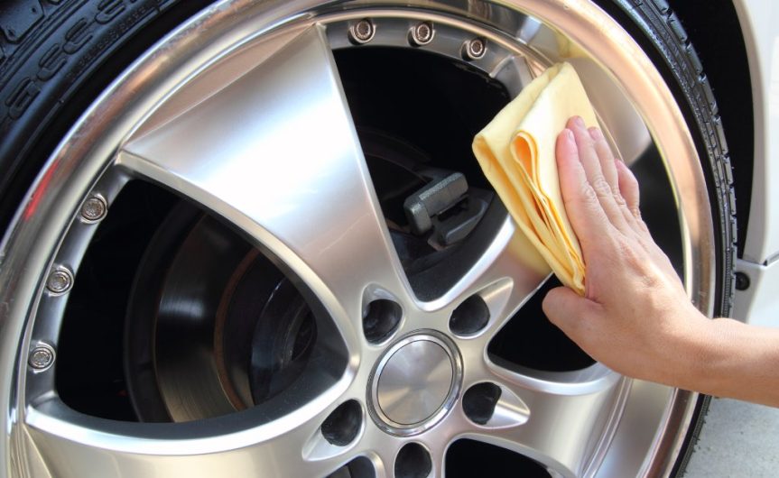 A person running a yellow microfiber cloth over a wheel that has been coated with a protective layer.