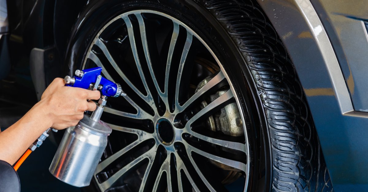 A person holding a spray canister is running a spray over a wheel. The spray bottle is metal with a blue handle.