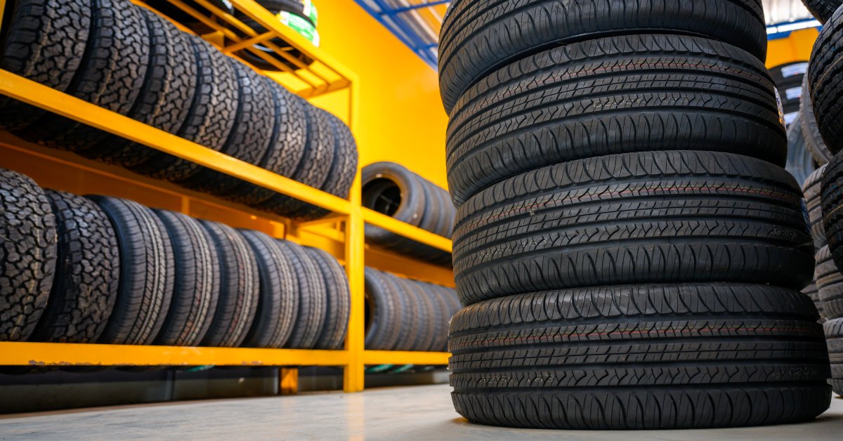 A warehouse with new tires stacked in different areas. One set is stacked on the floor, while others are on shelves.