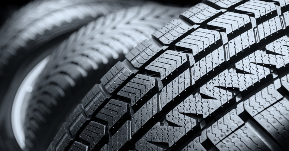 An unused car tire with a clear few of the tread and ridges. Behind it are other rows of similar tires.