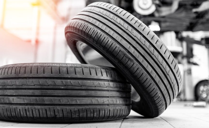 A tire on the floor with another tire leaning on it. Behind them is a blurred elevated vehicle in the background.