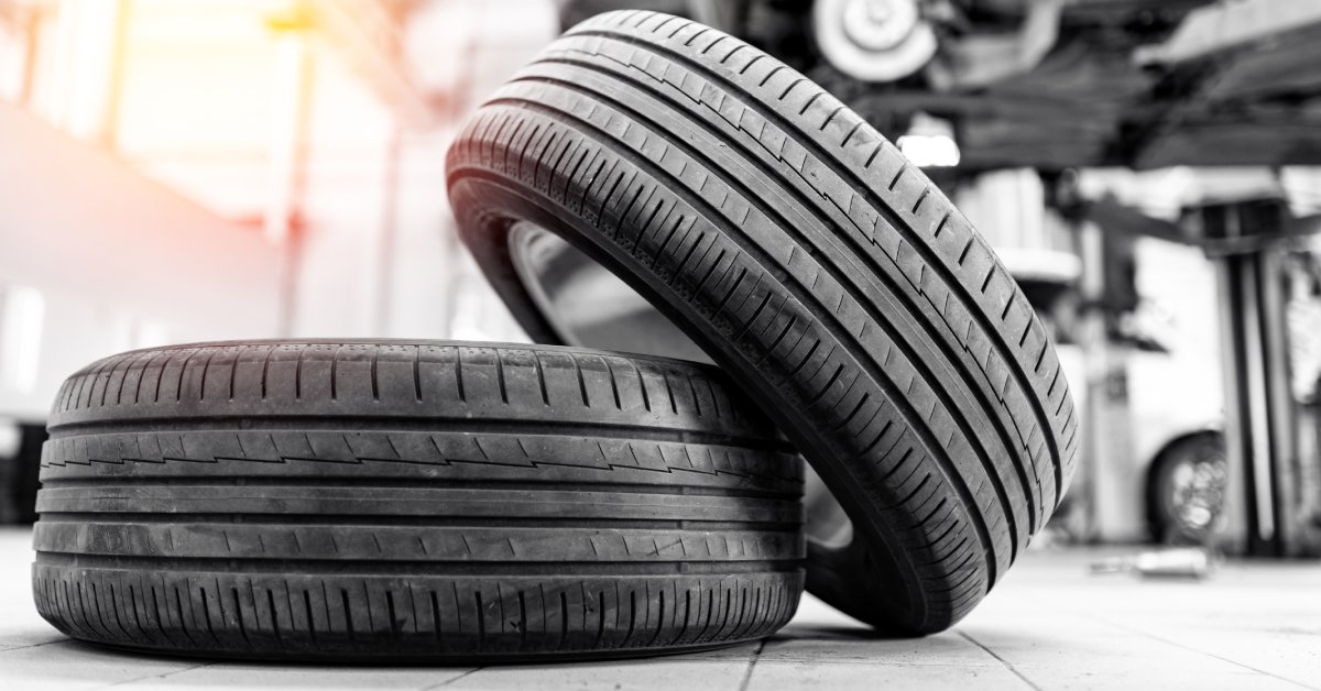 A tire on the floor with another tire leaning on it. Behind them is a blurred elevated vehicle in the background.