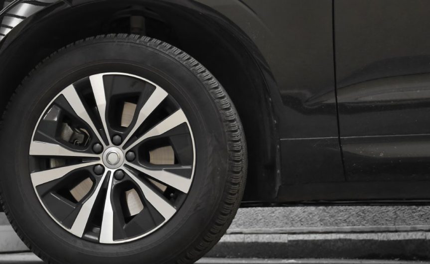 The bottom part of a modern black car with a tire attached to it. The vehicle is parked on a residential road.