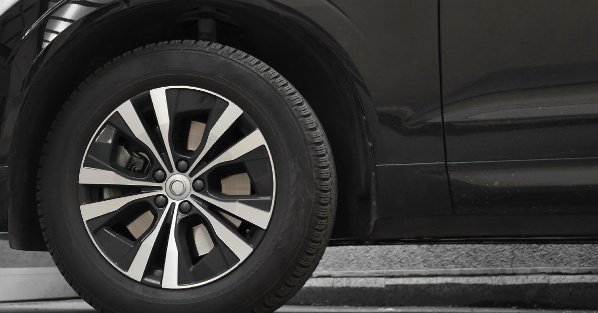 The bottom part of a modern black car with a tire attached to it. The vehicle is parked on a residential road.