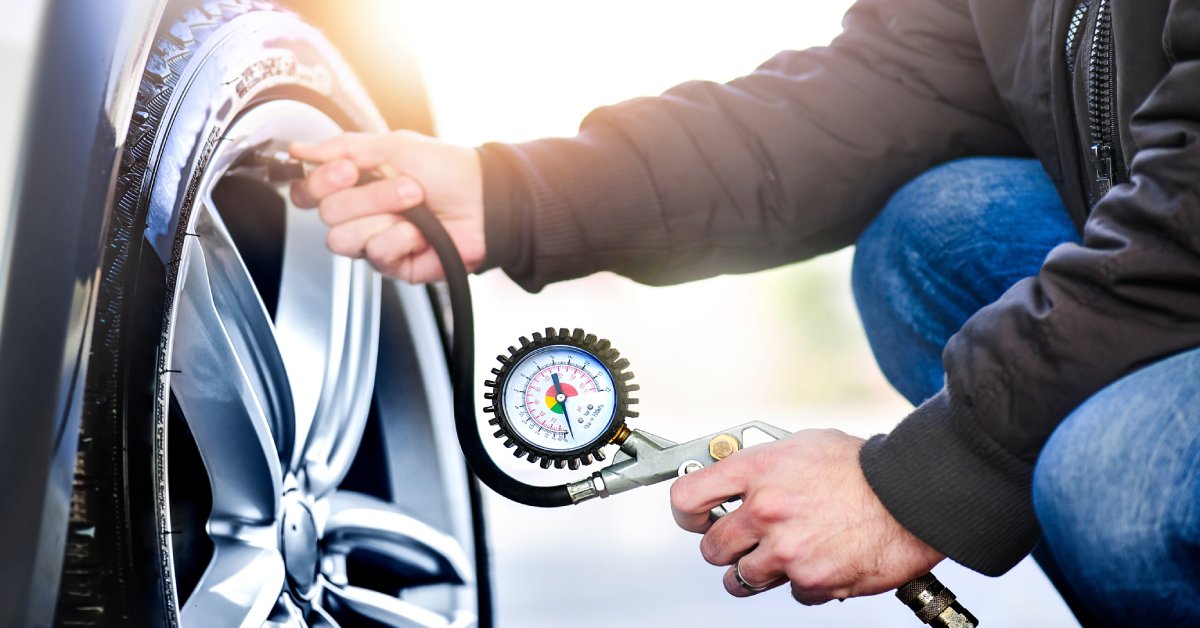 A person crouched next to a car with an air pump to inflate the tire. The tire pressure gauge is also visible.