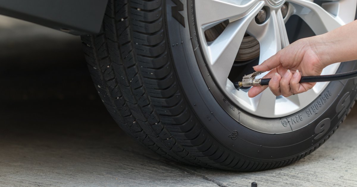 The bottom part of a tire with a person's hand holding an air pump. The pump is attached to the valve to fill the tire.