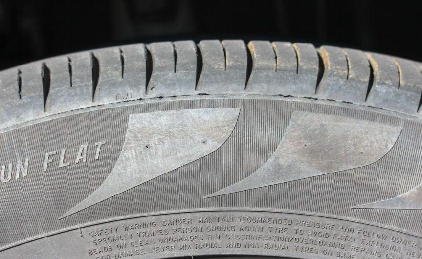 The side of a dirty run-flat tire. The sidewall features a design, and the words 
