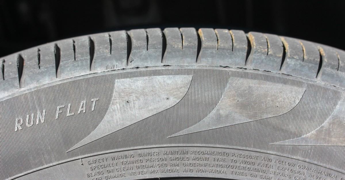 The side of a dirty run-flat tire. The sidewall features a design, and the words 