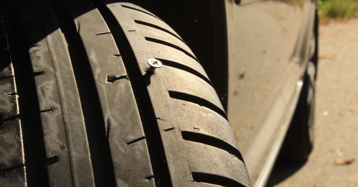 A tire turned outwards from under a vehicle. Next to the tread of the run-flat tire, a screw protrudes.