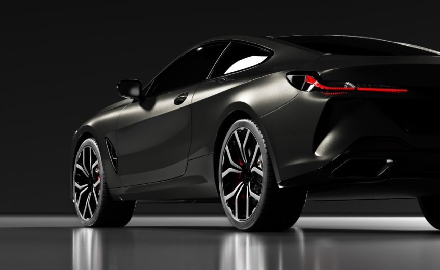 The rear part of a black modern car has a light shining on it. The vehicle is set against a black background.