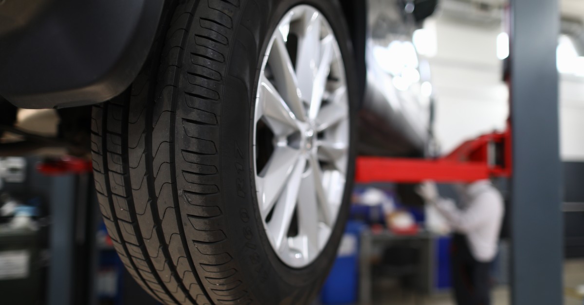 A close-up view of a grey car lifted in a maintenance shop sows the intricate details of the rear tire.