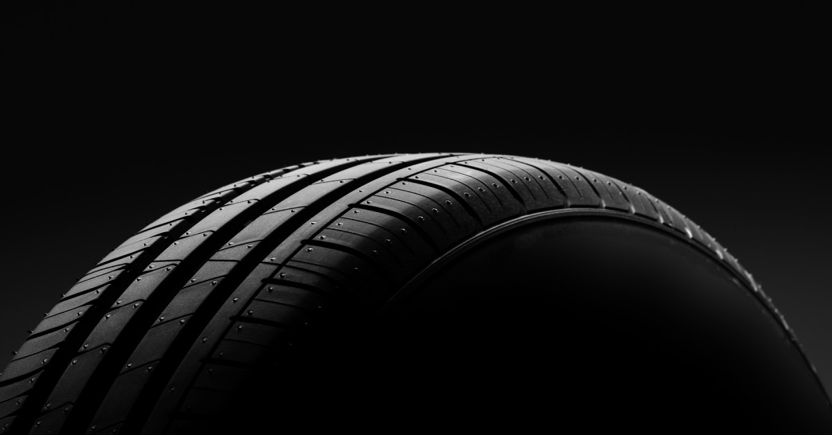 A close-up of a single car tire with detailed tread patterns, lit dramatically against a black background for contrast.