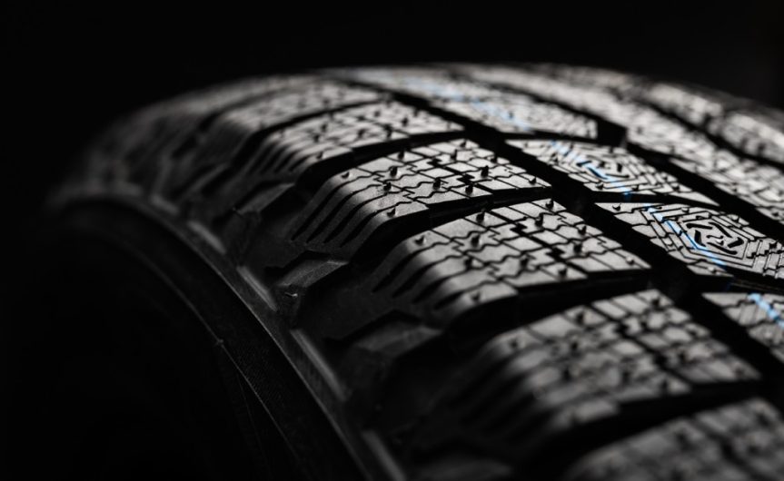 A new winter tire on a black background with a light illuminating the individual parts of the tread pattern.