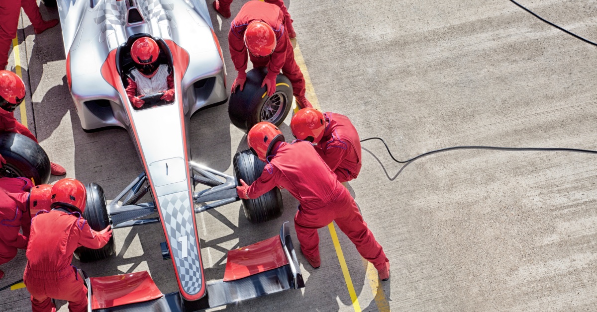 A racing team in red works on a car during a pit stop. The driver sits behind the wheel of the race car.