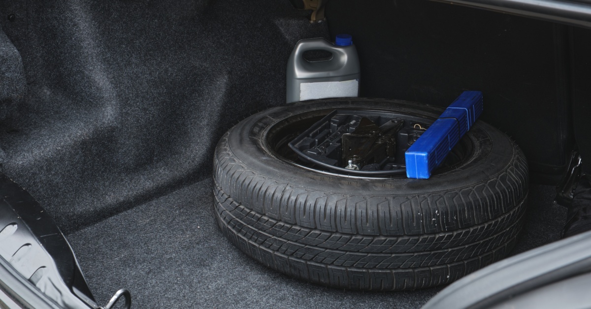 The interior of a car trunk with dark gray fabric, which holds a spare tire and a gray can behind it.