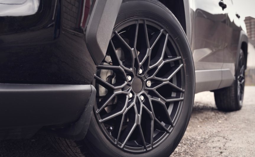 The lower half of a sleek, black car parked on a gravel road. The tires are clean and turned inward.