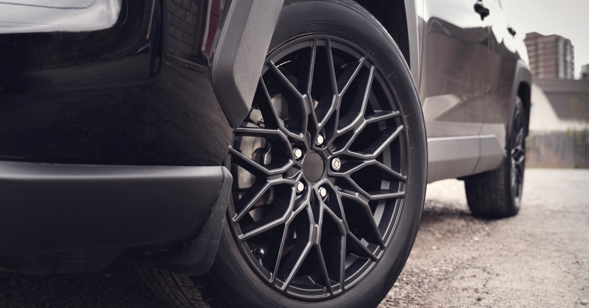The lower half of a sleek, black car parked on a gravel road. The tires are clean and turned inward.