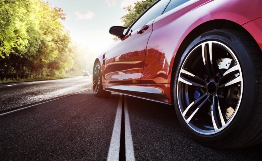 A shiny red sports car parked on the road. It is set across the white line and partially in the sunlight.
