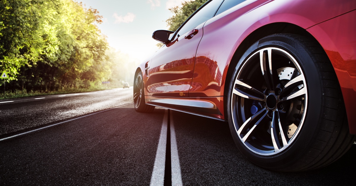 A shiny red sports car parked on the road. It is set across the white line and partially in the sunlight.