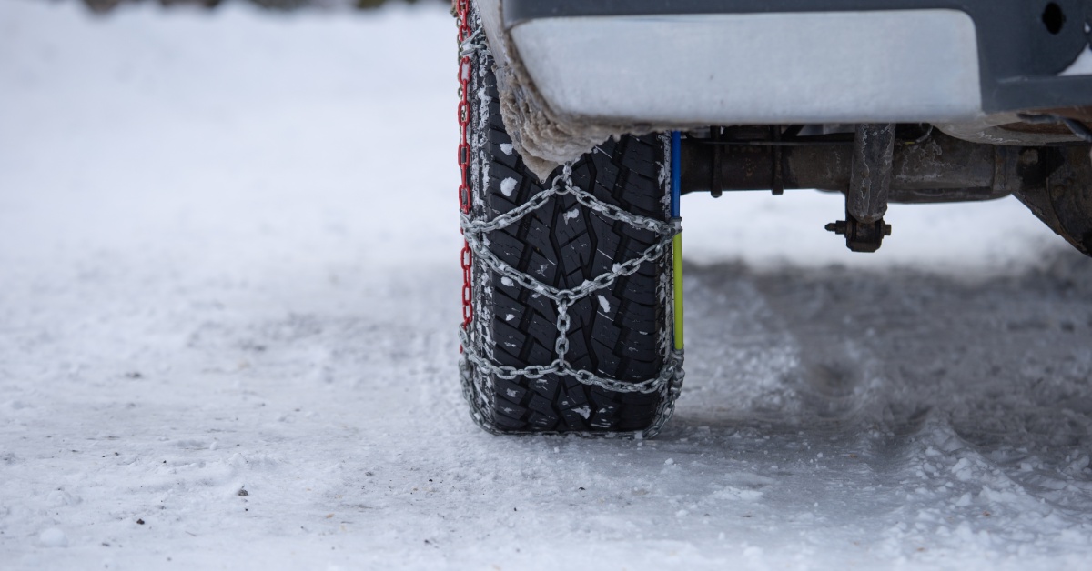A car's tire has red, blue, yellow, and silver snow chains installed on it to help with driving on snowy roads.