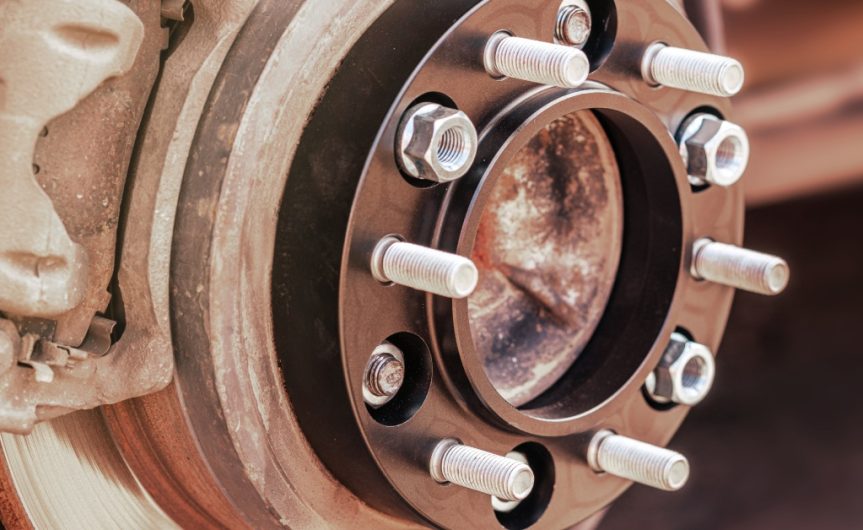 A wheel spacer mounted to the wheel hub of a car with screws and bolts sticking out to attach to the tire.