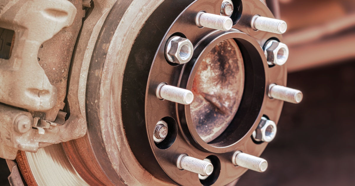 A wheel spacer mounted to the wheel hub of a car with screws and bolts sticking out to attach to the tire.