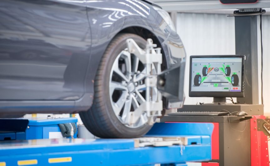 A modern car on a hydraulic lift in an auto shop with a computer showing tire information in the background.
