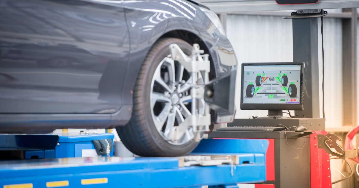 A modern car on a hydraulic lift in an auto shop with a computer showing tire information in the background.