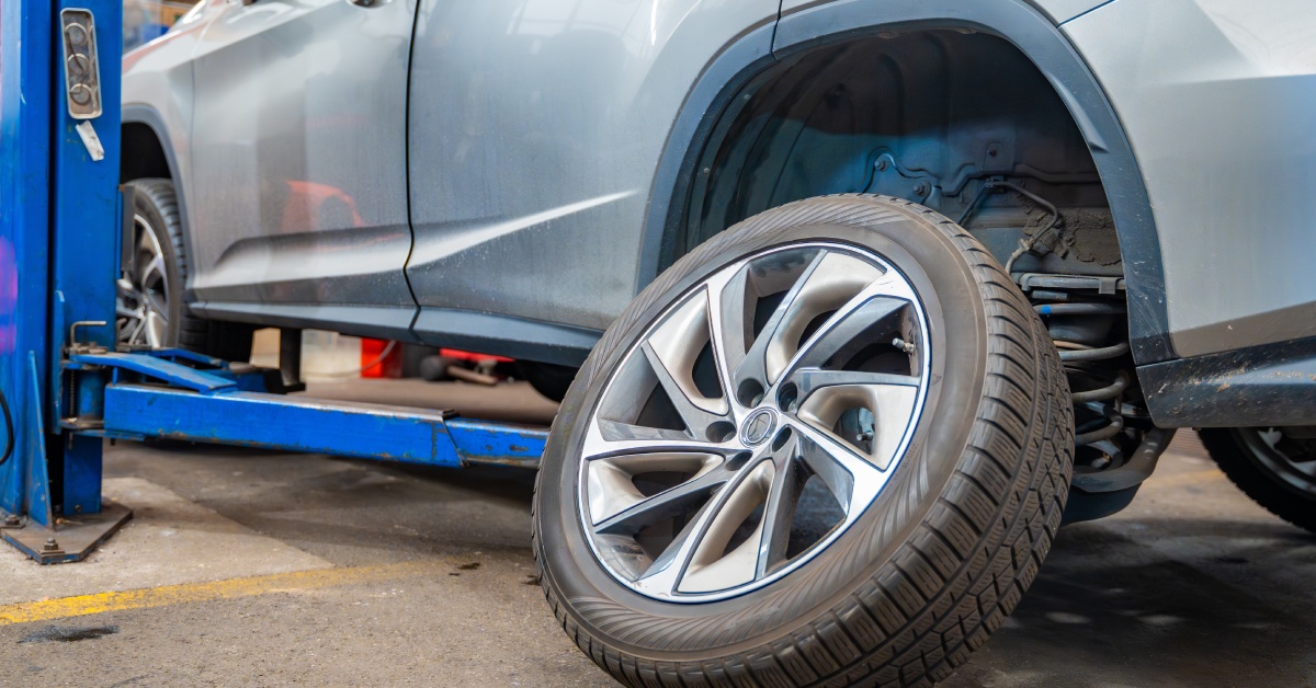 A low view of a modern car on a hydraulic lift with the rear wheel and tire removed from the wheel well.
