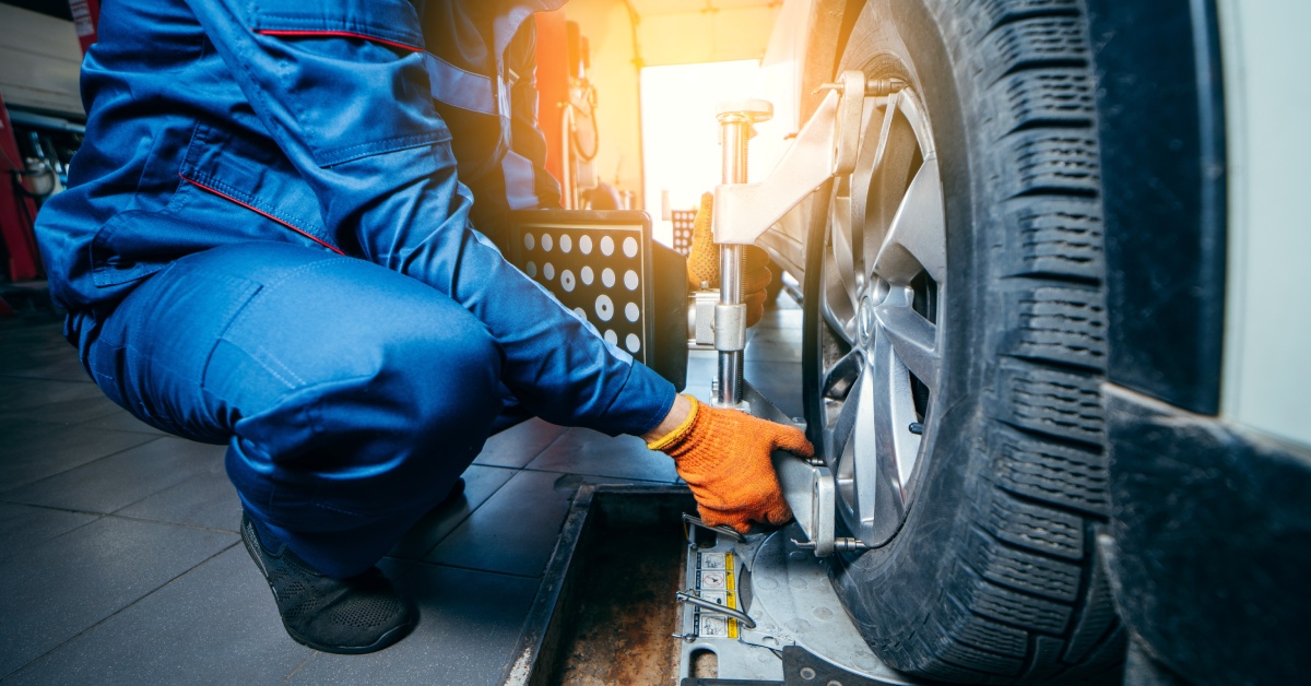 A close-up of an auto mechanic in a blue jumpsuit installing a sensor during a suspension adjustment on a car.