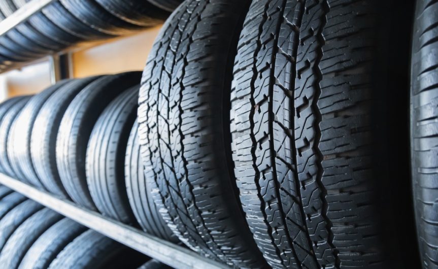 A close-up of new car tires on the middle row of a metal rack in an auto store with more rows of tires above and below.