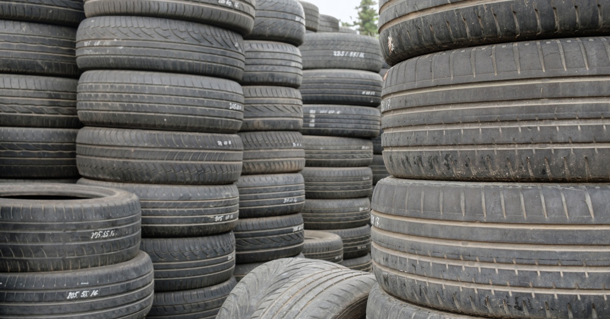 Numerous stacks of old automotive tires, stacked vertically on top of one another, in an empty lot during the day.