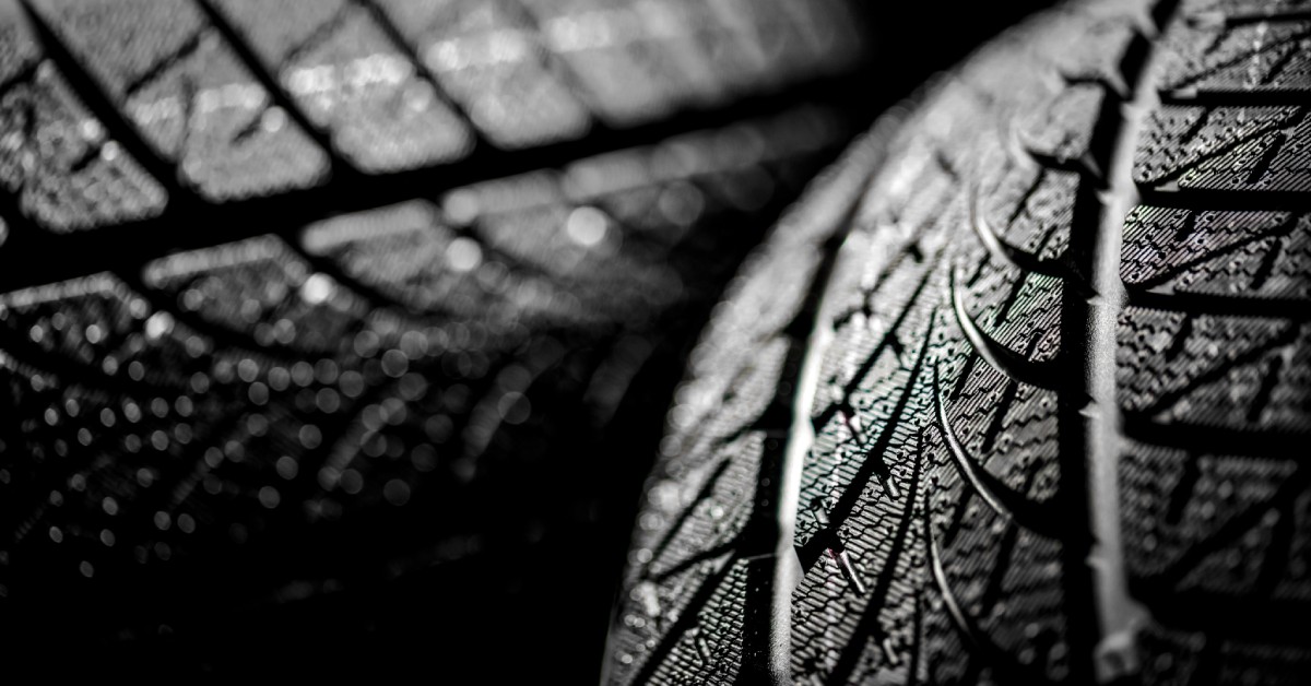 Two identical car tires placed side by side, under harsh lighting and against a pitch black background.