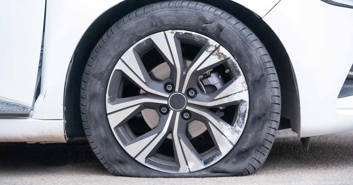 A clean white car with a flat tire. The bottom of the tire is deflated, and the rims have small marks.