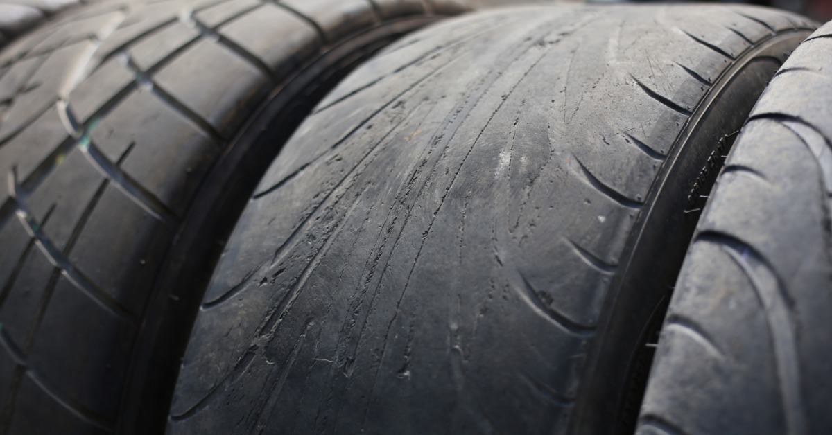 A close-up of an automotive tire with the tread almost completely worn down next to a new tire with fresh tread.